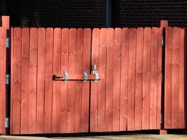 A pair of stained wood gates hung on a brick opening, with a metal drop latch.