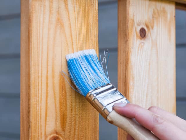 A brush laying protective stain along the grain of a fence board.