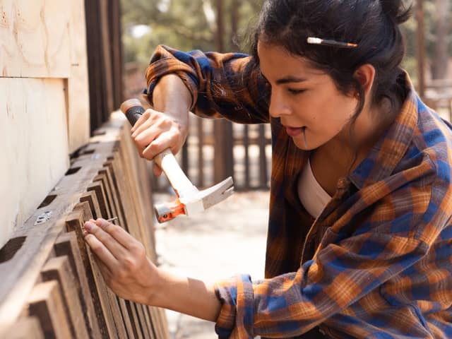 A carpenter hammering a replacement board into an existing wood fence.